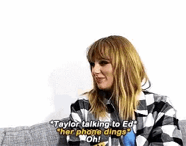 taylor swift is sitting on a couch talking to ed and her phone dings .