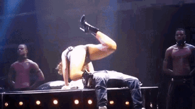 a woman is doing a handstand on a man 's lap on a stage