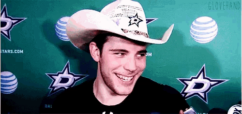 a man wearing a cowboy hat is smiling in front of a banner that says glovehand