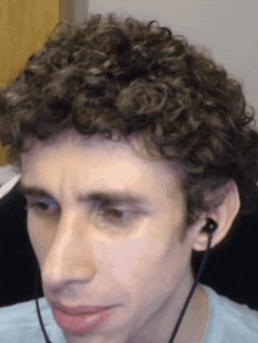 a man with curly hair wearing ear buds looks at the camera