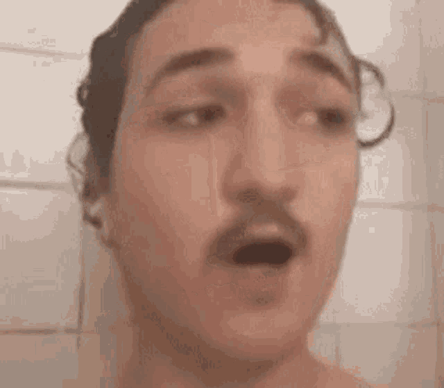 a man with a mustache is taking a shower and making a surprised face .
