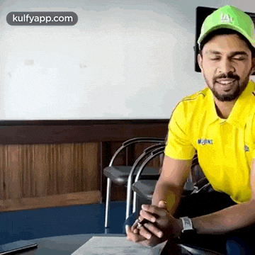 a man wearing a yellow shirt and a green hat is sitting at a table with his eyes closed .