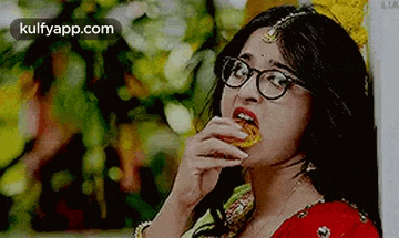 a woman wearing glasses is eating a piece of food from a plate .