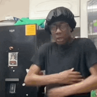 a man wearing a hat and glasses is standing in front of a refrigerator .