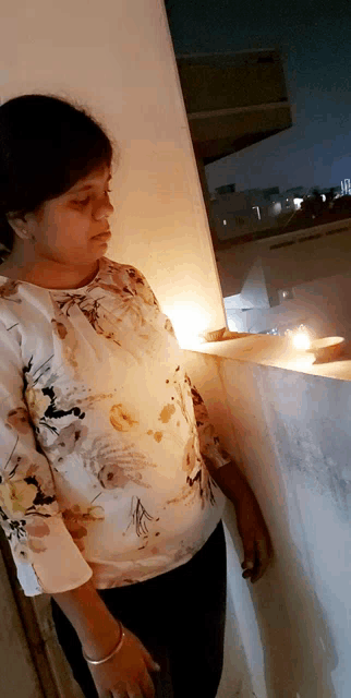 a woman in a floral shirt is standing in front of a wall with a lit candle