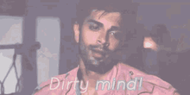 a man with a beard is wearing a pink shirt with the words `` dirty mind '' written above him .