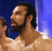 a shirtless man with a beard looks at something