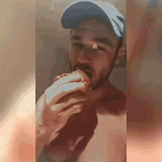 a man with a beard wearing a blue hat is eating a hamburger