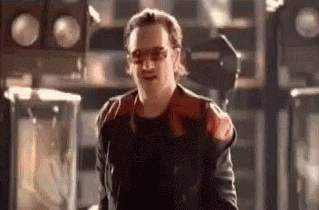 a man in a red and black jacket and sunglasses is standing in a room .