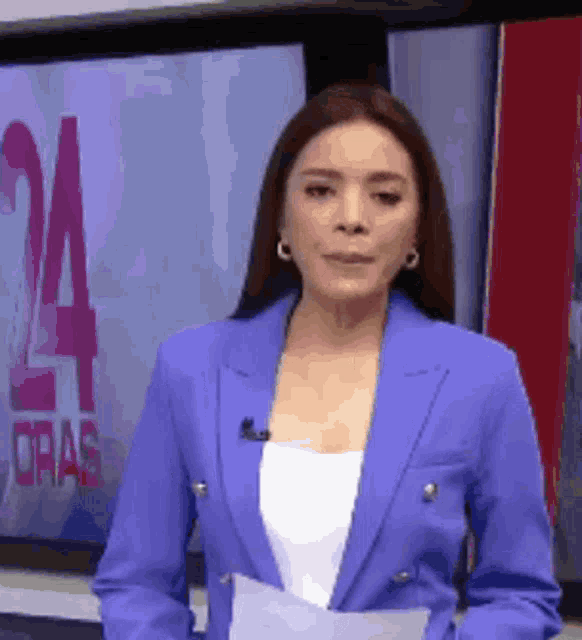 a woman in a blue jacket is standing in front of a television screen with the number 24 on it .