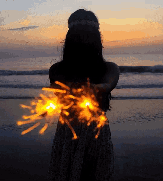 a woman holding sparklers in her hands on the beach