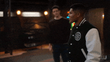 a man wearing a black and white varsity jacket with a circle logo on the back
