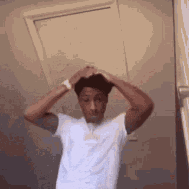 a man in a white shirt is adjusting his hair in front of a door .