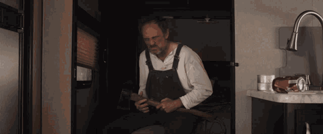 a man in overalls sits in a dark room holding a hammer