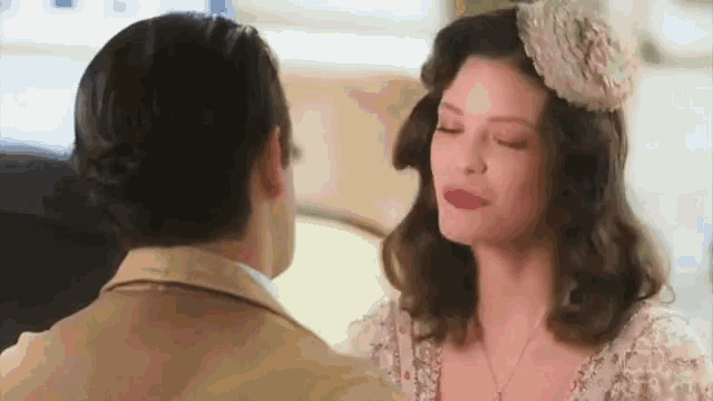 a man and a woman are looking at each other and the woman is wearing a hat .
