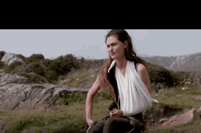 a woman with a bandage on her arm is sitting on a rock