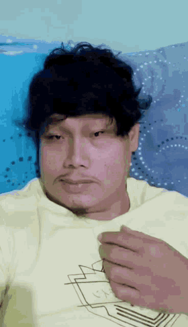 a man in a yellow shirt is laying on a bed with his hand on his chest .