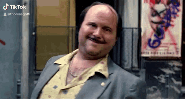 a bald man with a mustache wearing a suit and a yellow shirt is smiling .