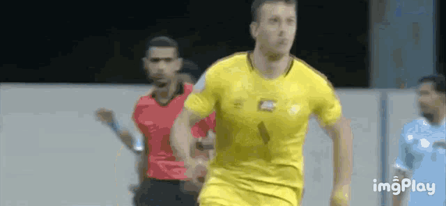 a man in a yellow shirt is running on a soccer field while a referee watches .