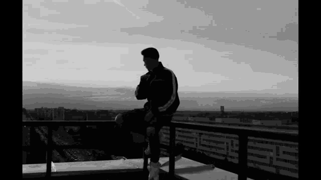 a black and white photo of a man sitting on the edge of a building .