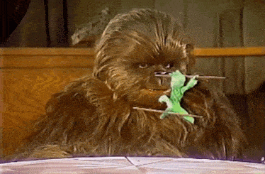 a chewbacca is holding a green toy in its mouth .