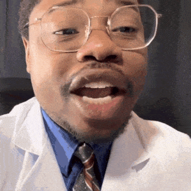 a man wearing glasses and a lab coat makes a funny face