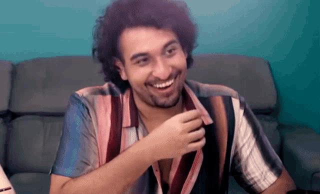 a man with curly hair and a beard is sitting on a couch and smiling .