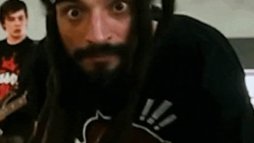 a man with dreadlocks and a beard is wearing a bandana and making a funny face .