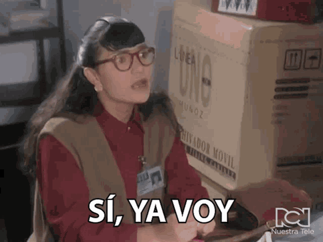 a woman with glasses says si ya voy in front of a cardboard box