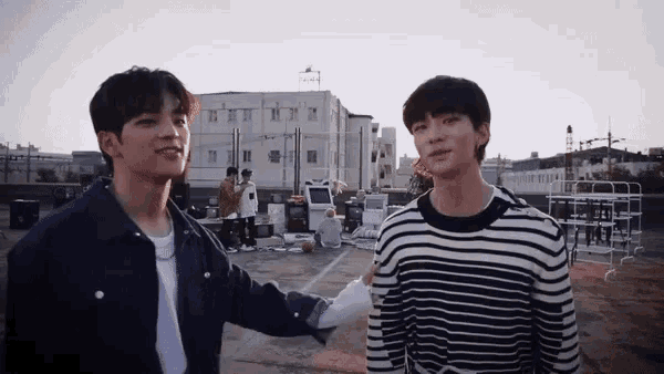two young men are standing next to each other on a rooftop and talking to each other .