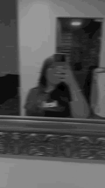 a black and white photo of a woman taking a selfie in front of a mirror .
