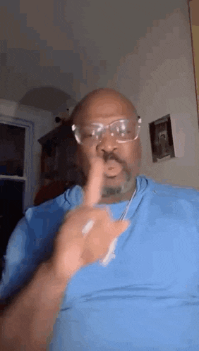 a man wearing glasses and a blue shirt is giving a thumbs up .