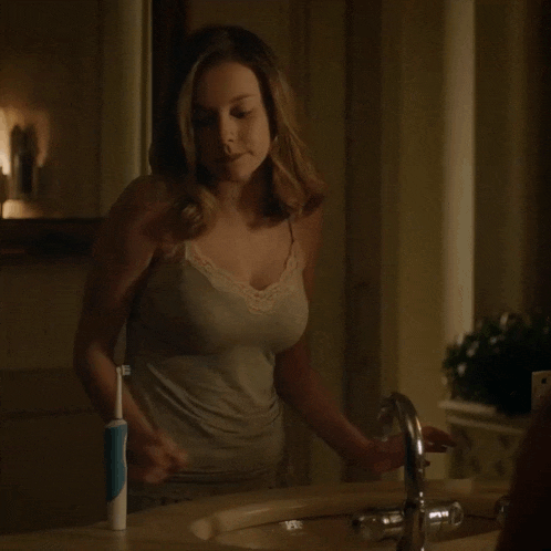 a woman standing in front of a sink with a toothbrush