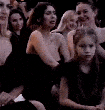 a woman in a black dress is talking to another woman in a crowd of people .