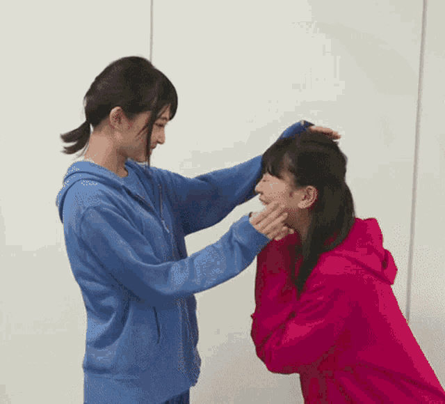 a woman in a blue hoodie is putting her hand on another woman 's face