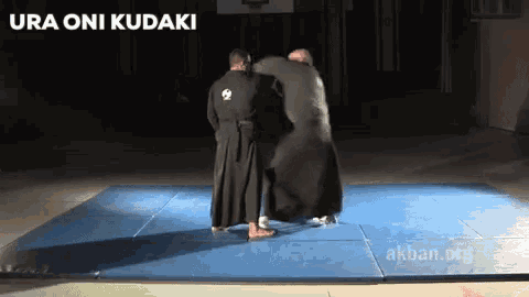 two men are standing on a blue mat with the words ura oni kudaki written above them