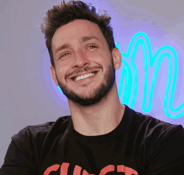 a man with a beard is smiling in front of a neon sign