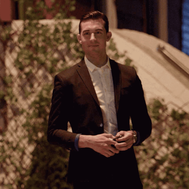 a man in a suit and white shirt is standing in front of a wall