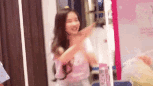 a woman in a pink shirt is standing in front of a mirror in a room .