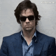 a man in a suit and sunglasses is standing in front of a white wall .