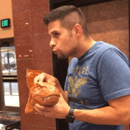 a man in a blue shirt is eating a t-rex shaped bag of chips .