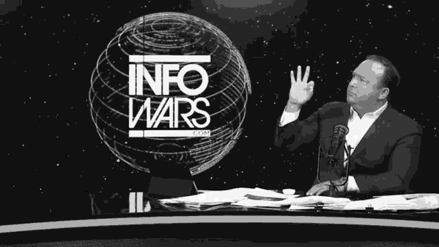 a man is sitting at a desk in front of a sign that says info wars