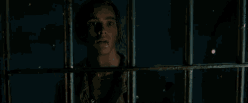 a man is behind bars in a dark room looking out of a window .