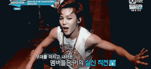 a young man is sitting on the floor with his arms outstretched in front of a tv screen that says mnet begins