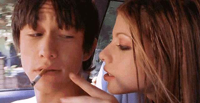 a woman is kissing a man on the cheek while he is smoking a cigarette .