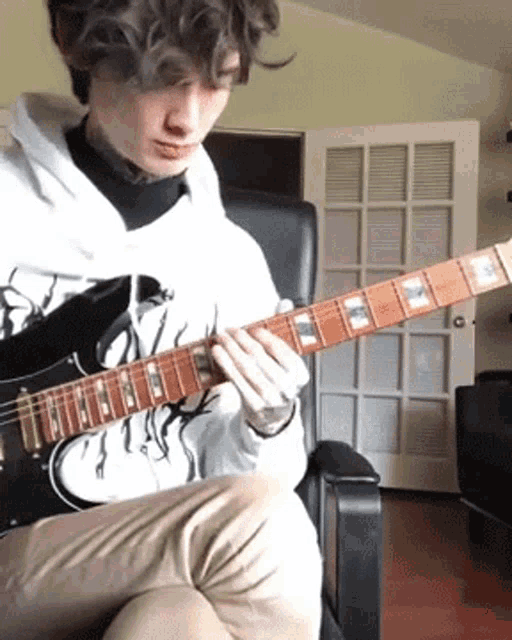a man in a white hoodie is playing an electric guitar