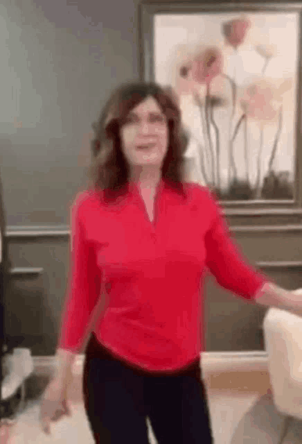 a woman in a red shirt is dancing in front of a painting in a living room .