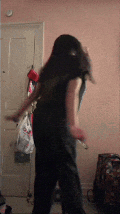 a woman in a black shirt is dancing in a room with a pink wall