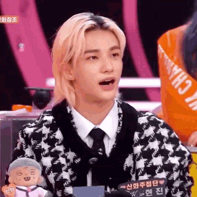 a young man with blonde hair is wearing a black and white sweater and tie and holding a stuffed animal .