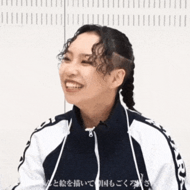 a woman with braids and a shaved head is smiling and wearing a black and white jacket